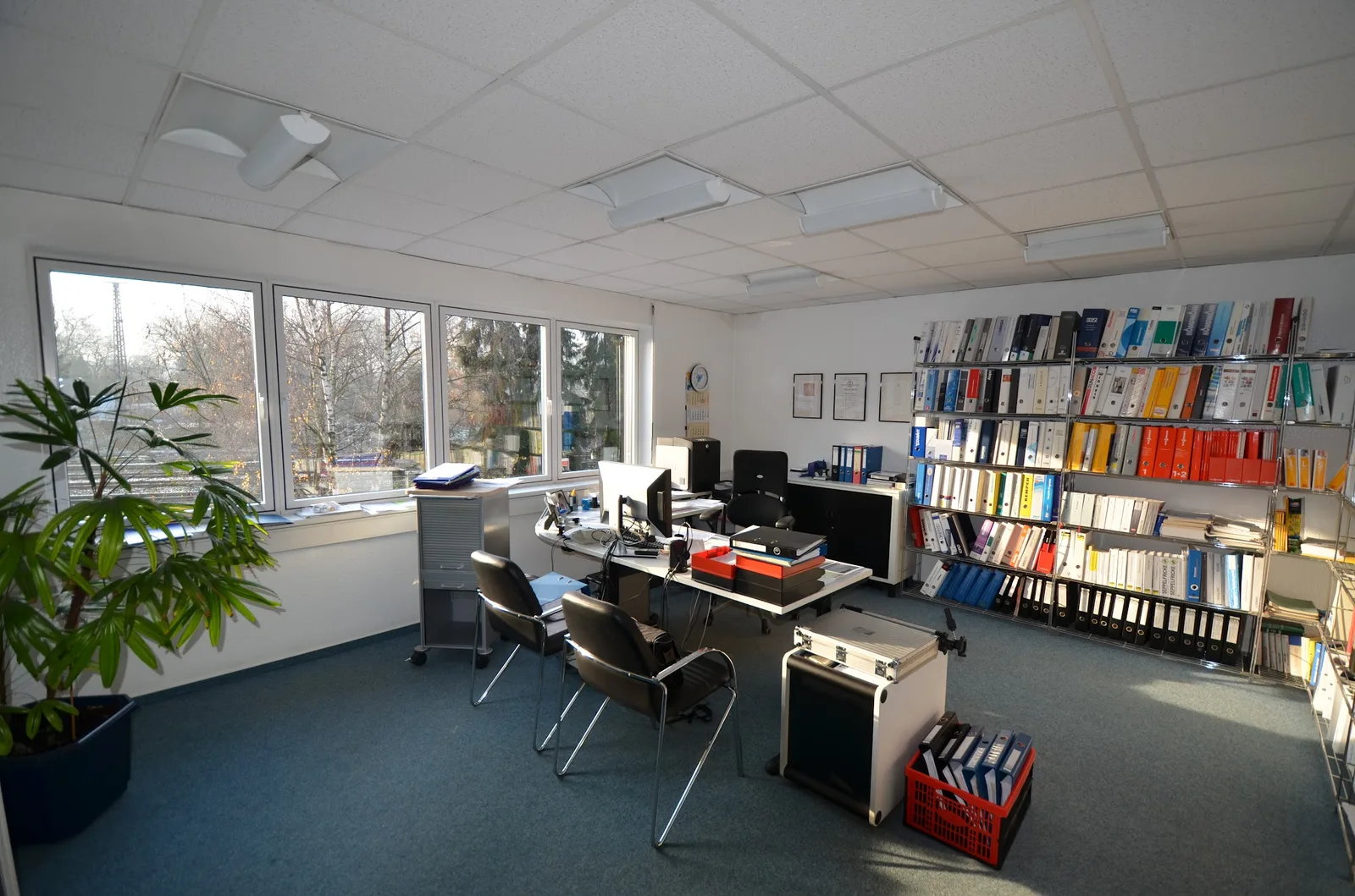 Helles Büro mit Fensterfront, Schreibtisch und Regalen voller Ordner